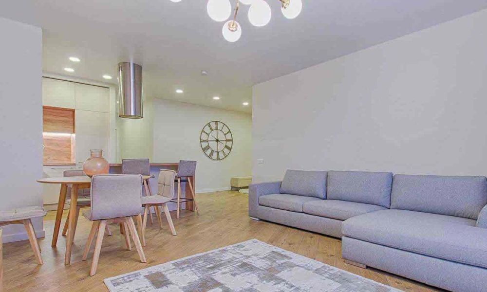 A modern living room with a gray sectional sofa, a dining area with a round table and chairs, and stylish lighting fixtures, creating a cozy and elegant ambiance.